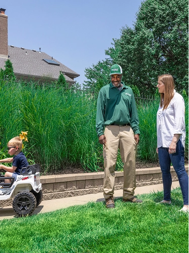 A smiling TruGreen technician stands proudly on a healthy, vibrant green lawn. 